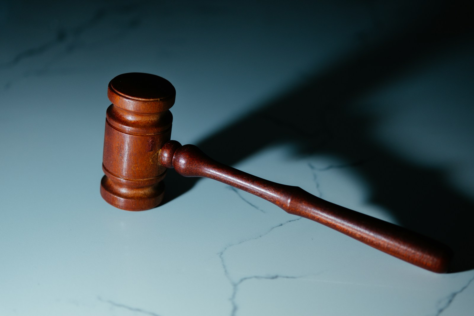 Wooden judge's gavel resting on a marble table in dark, teal-toned light